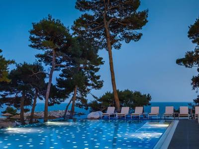 Verlicht zwembad met ligbedden en bomen bij zonsondergang in het hotel.