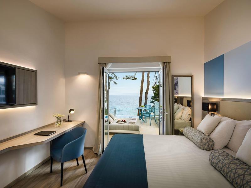 Moderní hotelový pokoj s výhledem na moře, manželskou postelí, pracovním stolem a terasou.