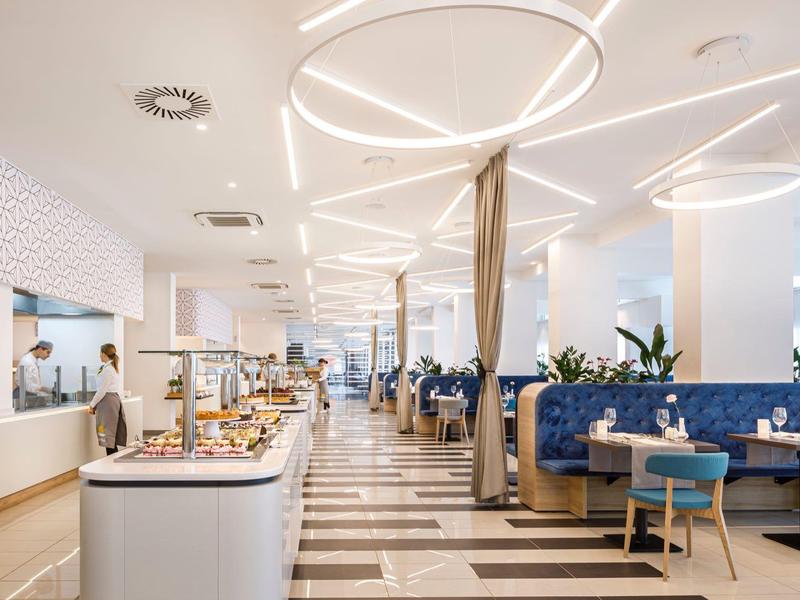 Moderní, světlá hotelová restaurace s bufetem a stylovými modrými a dřevěnými posezeními.