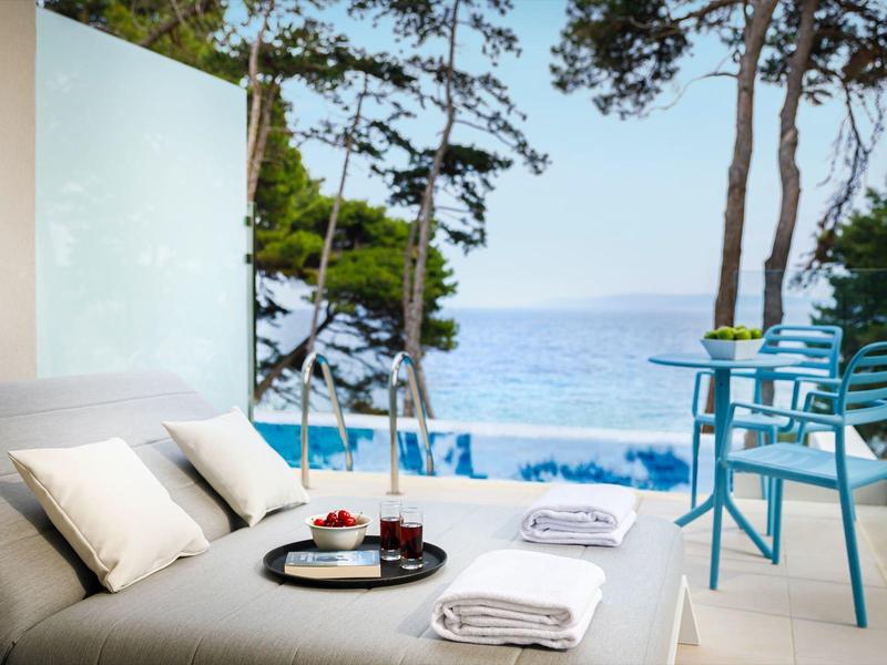 Terasa s posezením s výhledem na bazén a moře, obklopená stromy.