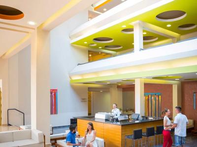 Modern hotel lobby with seating, a central desk, and colorful ceiling accents.