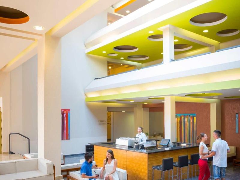 Modern hotel lobby with seating, a central desk, and colorful ceiling accents.
