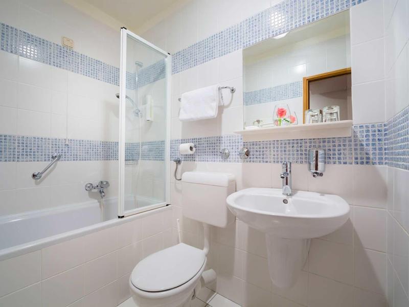 Compact bathroom with bathtub, shower screen, toilet, pedestal sink, and tiled walls.