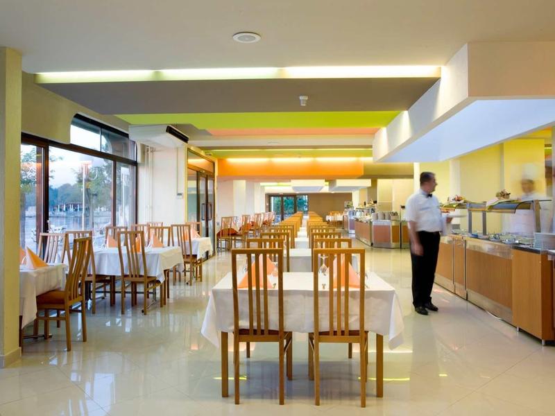 Spacious hotel dining area with wooden chairs, buffet setup, and large windows providing natural light.