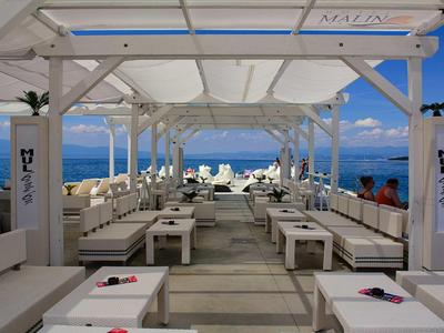 Moderno club de playa blanco con sillas y mesas con vista al mar al atardecer.