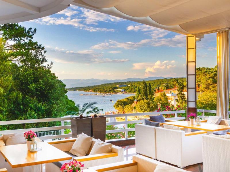 Terrazza con area salotto che si affaccia sul mare e colline boscose sotto un cielo sereno.