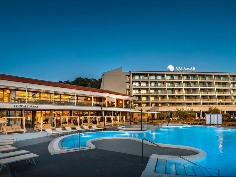 Nowoczesny kompleks hotelowy z oświetlonym basenem o zmierzchu i jasnym niebieskim niebem.