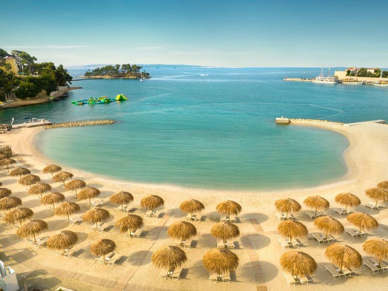 Plaża z rzędami słomianych parasoli i czystą, spokojną wodą w słoneczny dzień.