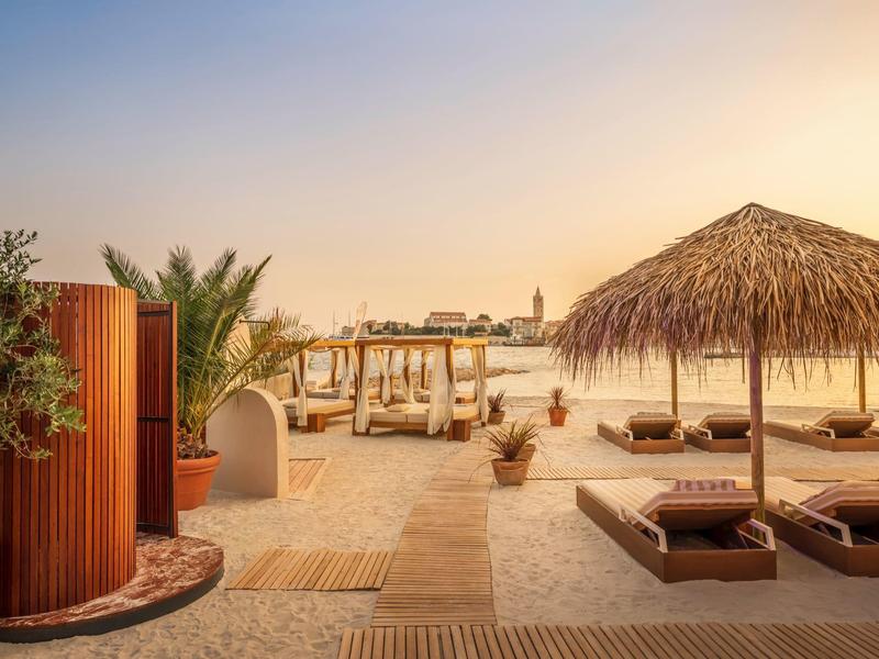 Plaża z leżakami, parasolami i palmami o zachodzie słońca w ośrodku hotelowym.