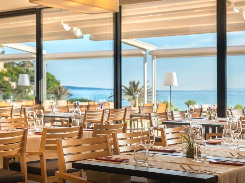 Jasna restauracja z drewnianymi meblami i widokiem na morze w słoneczny dzień.