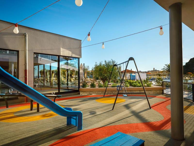 Nowoczesny plac zabaw z huśtawką i zjeżdżalnią na nasłonecznionym tarasie obok budynku.