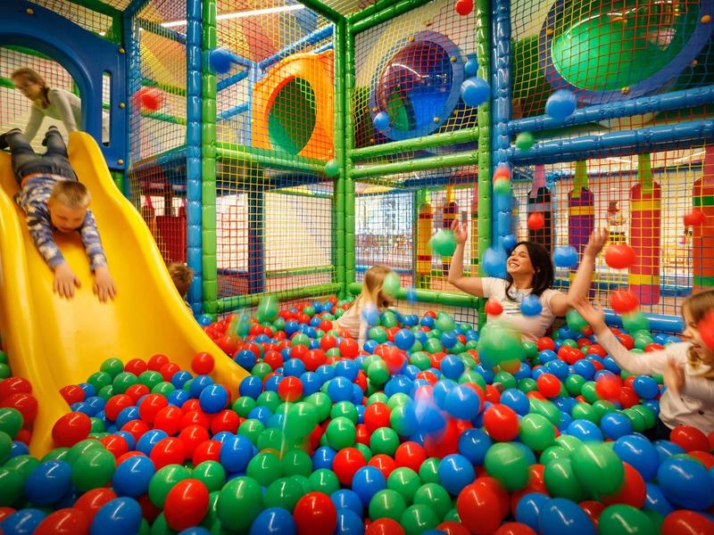 Dzieci bawią się w kolorowym basenie z piłeczkami ze zjeżdżalnią w sali zabaw.