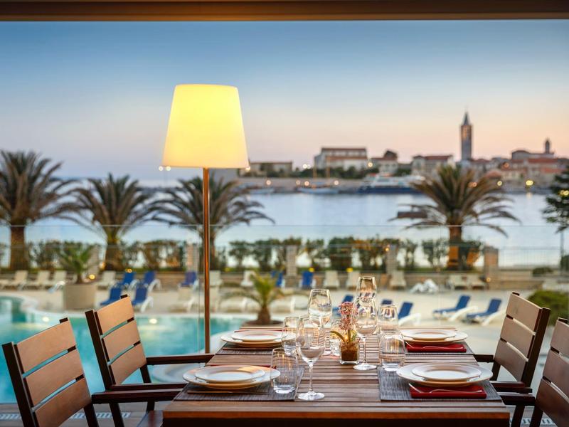 Elegancko nakryty stół z widokiem na basen i morze o zachodzie słońca.