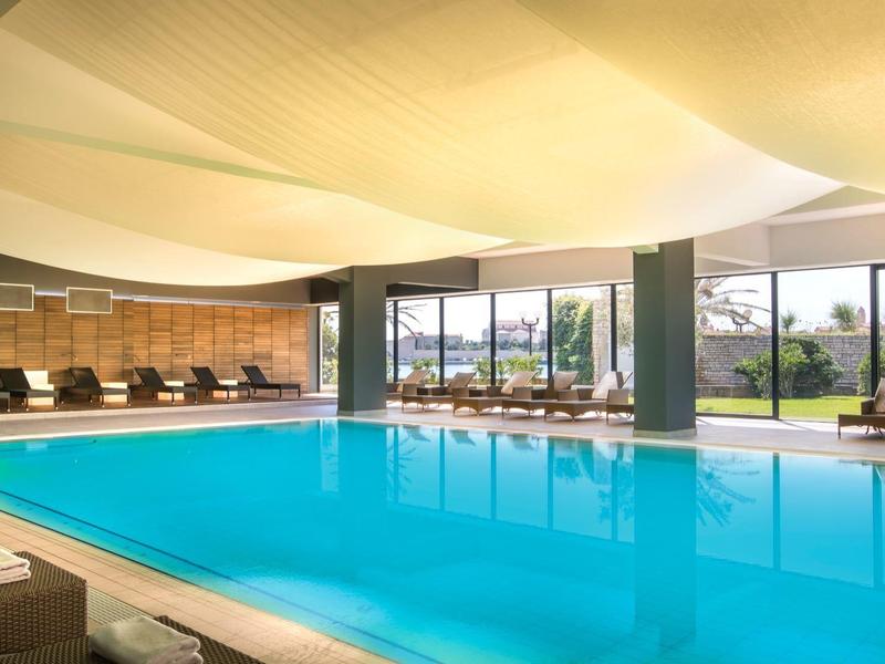 Wnętrze z dużym basenem, fotelami i dużymi oknami z widokiem na ogród.