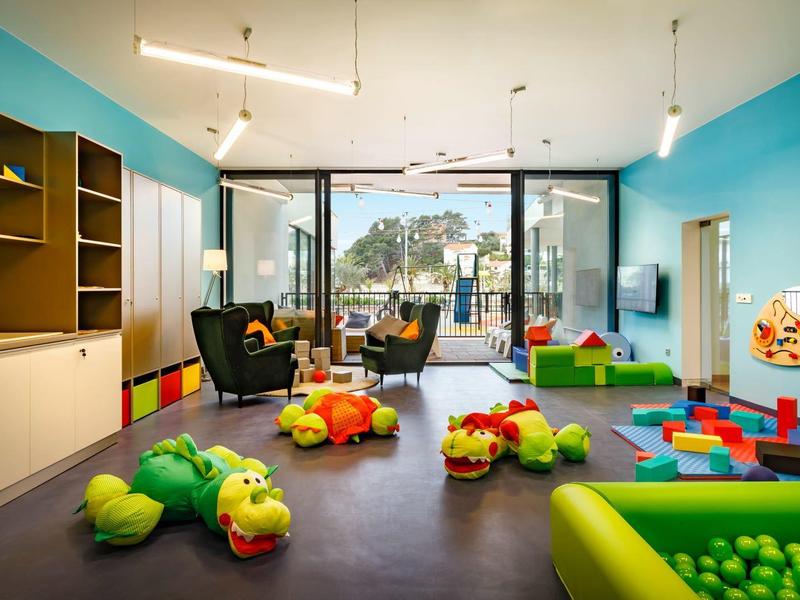 Jasny kącik zabaw dla dzieci z kolorowymi zabawkami i dużymi oknami w hotelu.