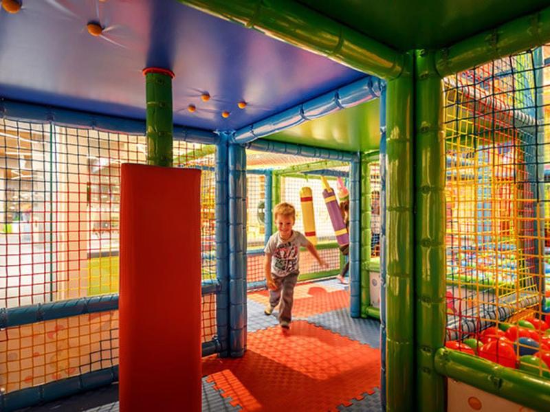 Dziecko bawi się w krytej sali zabaw z kolorowymi piłeczkami i piankowymi konstrukcjami.