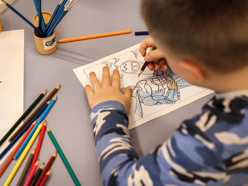 Dziecko koloruje rysunki kredkami na stole.