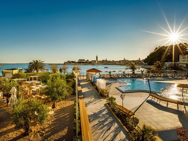 Zachód słońca nad basenem i ogrodem hotelu z widokiem na morze.