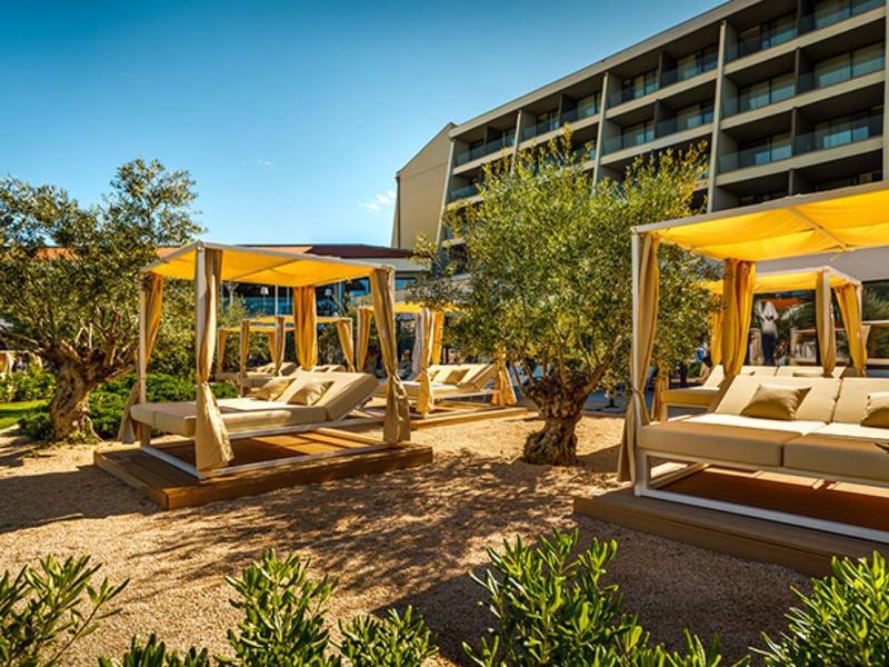 Strefa zewnętrzna hotelu z nowoczesnymi łóżkami lounge z żółtymi zadaszeniami i zielonym ogrodem.