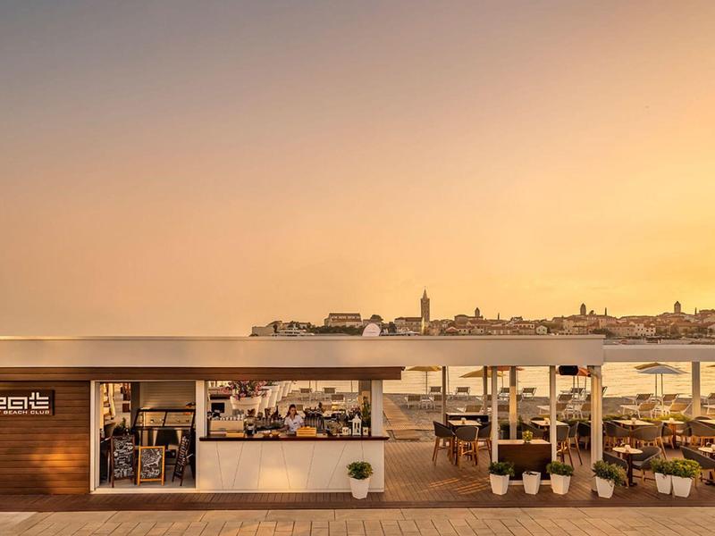 Nowoczesna restauracja na plaży z otwartą przestrzenią i panoramicznym widokiem na morze o zachodzie słońca.