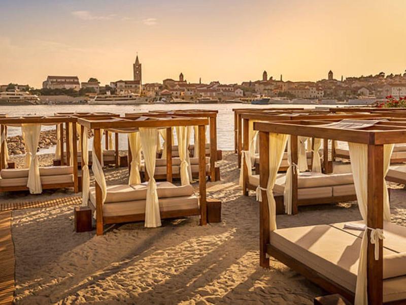 Leżaki na plaży z widokiem na miasto o zachodzie słońca.