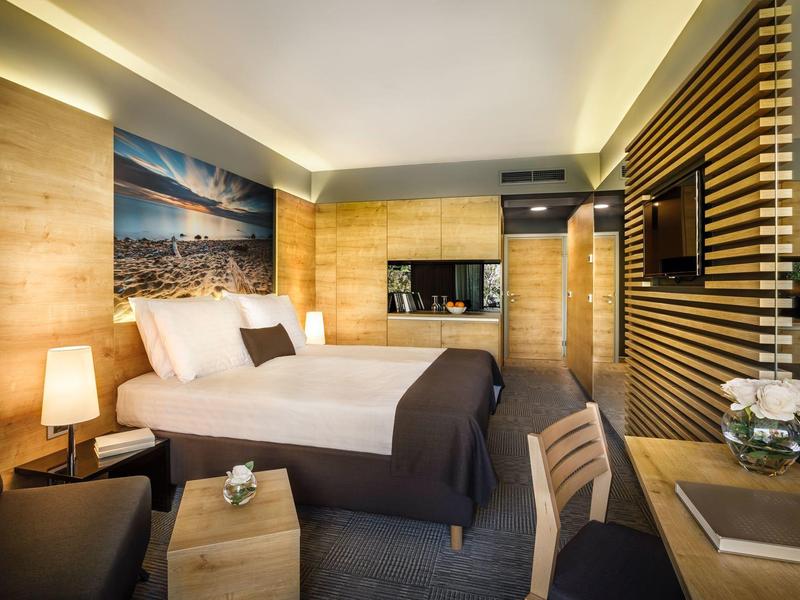 Nowoczesny pokój hotelowy z dużym łóżkiem, drewnianą lamperią i przytulnym oświetleniem.