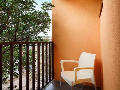 Balkon met witte stoel en oranje muur naast reling en bomen op de achtergrond.