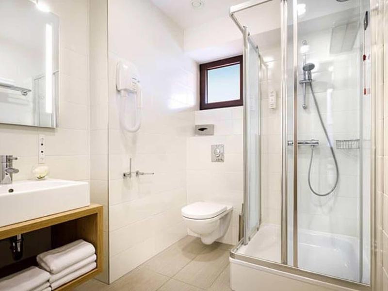 Lichte, moderne hotelbadkamer met douche, toilet, wastafel, handdoeken en föhn.