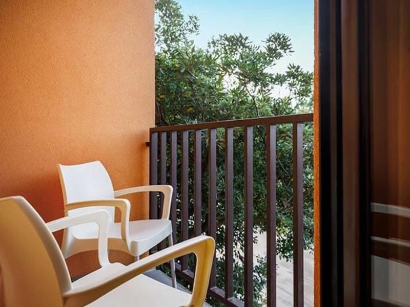 Balkon met witte stoelen en uitzicht op bomen achter een bruin hek.