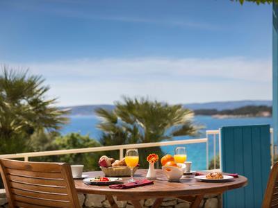 Table de balcon avec petit-déjeuner, vue sur la mer et les palmiers sous un ciel clair.