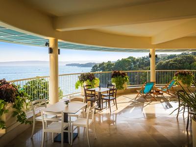 Terrasse couverte avec tables, chaises et vue sur la mer par temps ensoleillé.