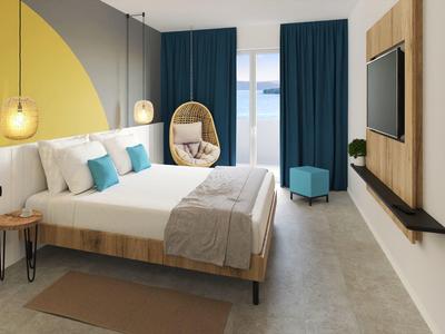 Moderní hotelový pokoj s manželskou postelí, modrými závěsy a závěsným křeslem u okna.