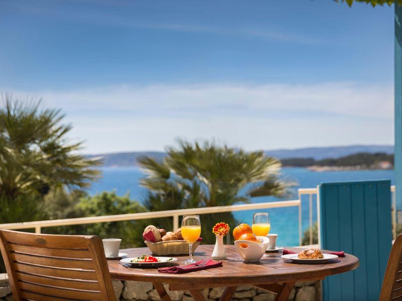 Stůl na snídani venku na balkoně s výhledem na moře a palmy.