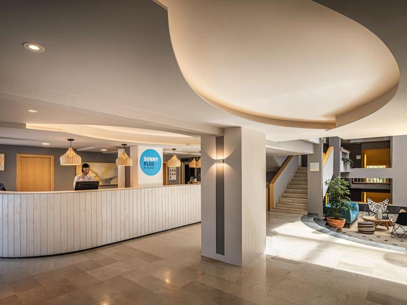 Moderní hotelová lobby s jasnou recepcí, designovým osvětlením a odpočinkovou zónou s rostlinami.