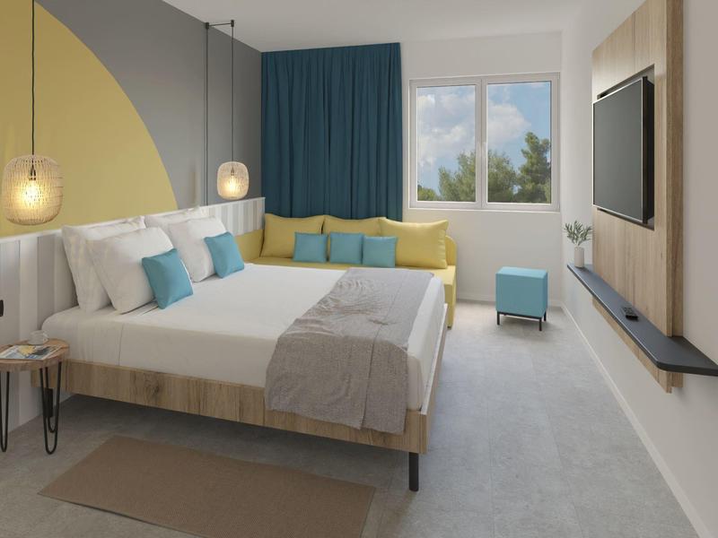 Moderní hotelový pokoj s manželskou postelí, žlutými a modrými akcenty a výhledem z okna.