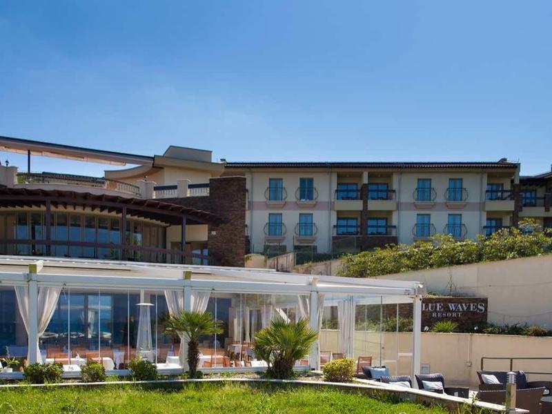 Complesso alberghiero moderno con prati verdi, padiglioni e un grande edificio sullo sfondo.