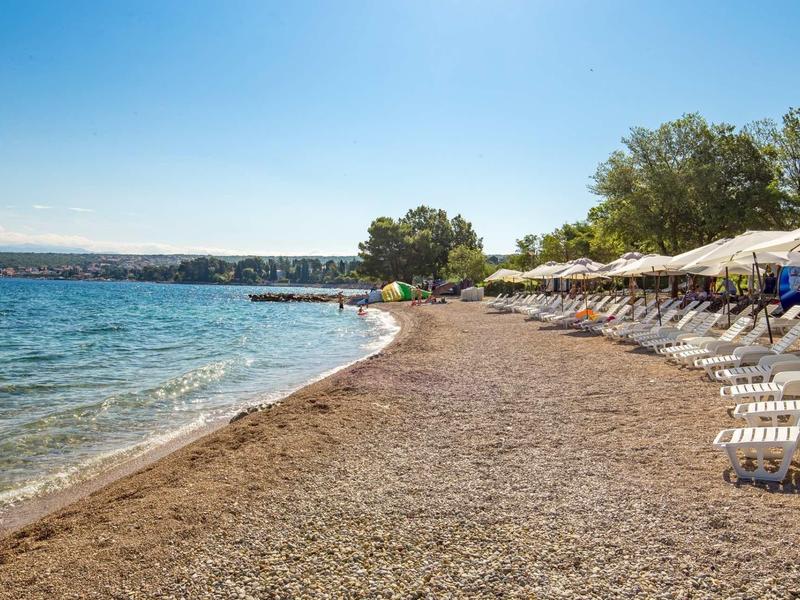 Spiaggia di ciottoli con sdraio e ombrelloni in una giornata tranquilla e soleggiata.