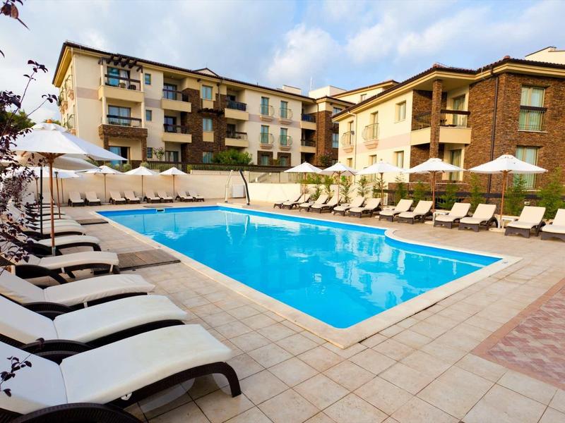 Piscina esterna moderna con lettini bianchi e ombrelloni davanti agli edifici dell'hotel.