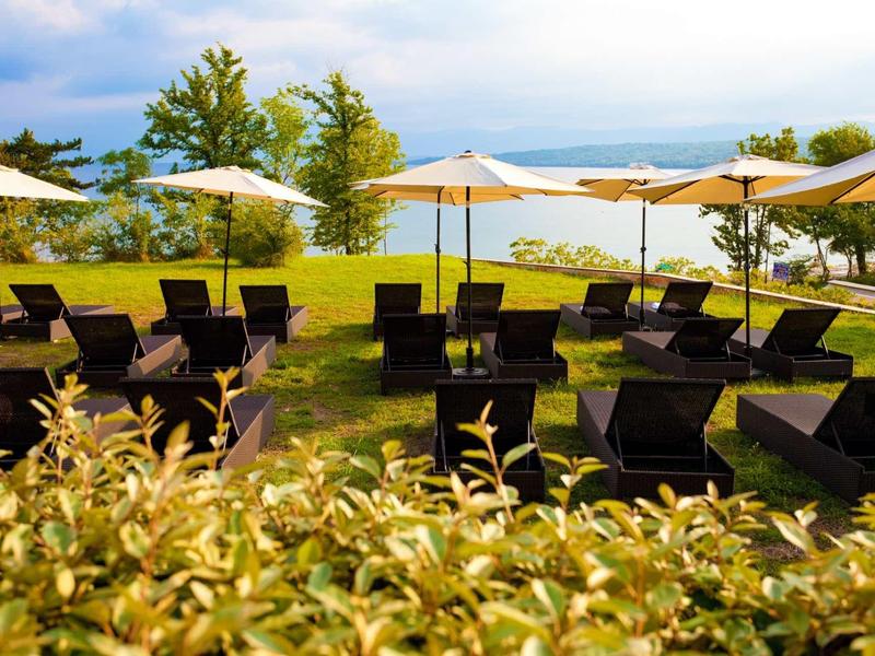 Lettini prendisole e ombrelloni su un prato verde con vista su un lago.