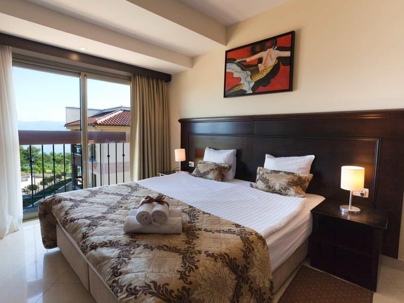 Camera d'hotel accogliente con letto, balcone e vista mare alla luce del giorno.