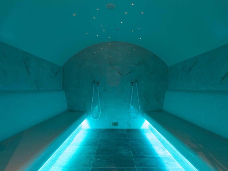 Scale illuminate conducono a una stanza hammam buia e voltata con panchine ai lati.