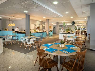 Ampia e luminosa sala da pranzo con sedie in legno e tavoli apparecchiati in un ristorante.