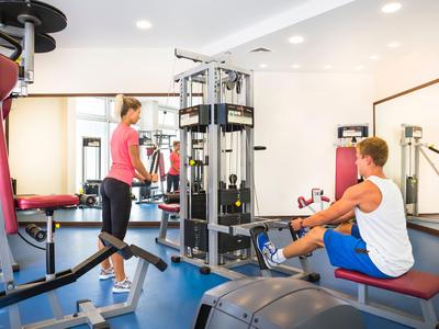 Due persone si allenano in una palestra moderna con attrezzature per forza e cardio.