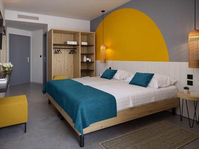 Chambre d'hôtel moderne avec grand lit, couvre-lit bleu et mur d'accent jaune.