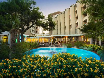 Hotel con fontana illuminata circondata da fiori e alberi al crepuscolo.