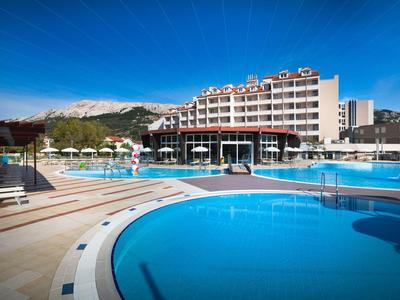 Großer Hotelkomplex mit mehreren Schwimmbecken und Bergen im Hintergrund unter blauem Himmel.