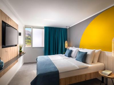 Chambre d'hôtel moderne avec grand lit et mur gris avec un demi-cercle jaune.