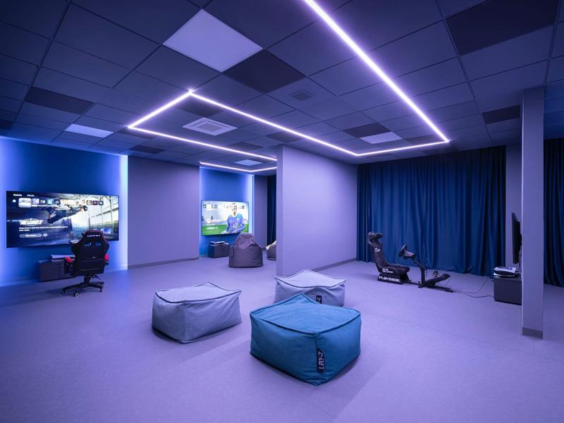 Salon moderne éclairé en bleu avec poufs, téléviseurs et rideaux.