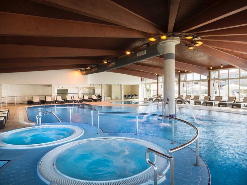Piscine intérieure avec jacuzzi chauffé dans un hôtel moderne avec grandes fenêtres et espaces assis.
