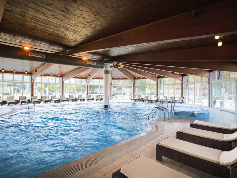 Piscine intérieure avec chaises longues confortables et grandes fenêtres laissant entrer la lumière du jour.